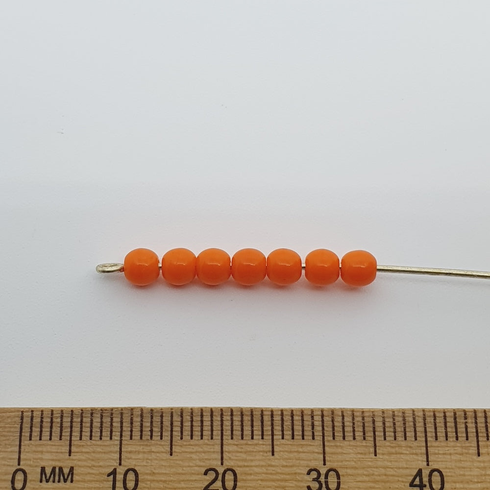 Opaque orange round beads on a pin with a ruler for scale on a white background