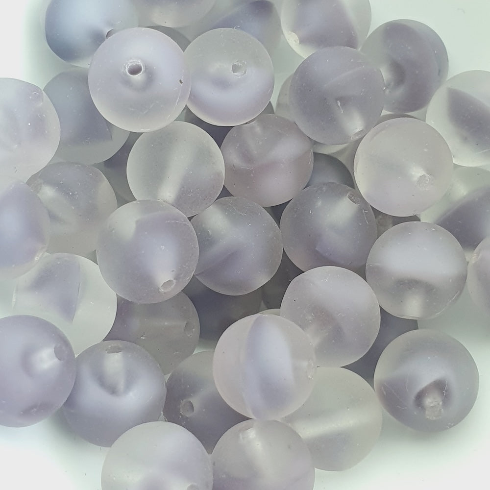 A collection of round, clear glass beads with a milky purple tint.