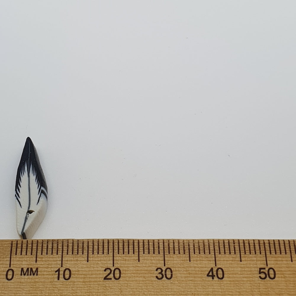Small feather bead next to a wooden ruler on a white background