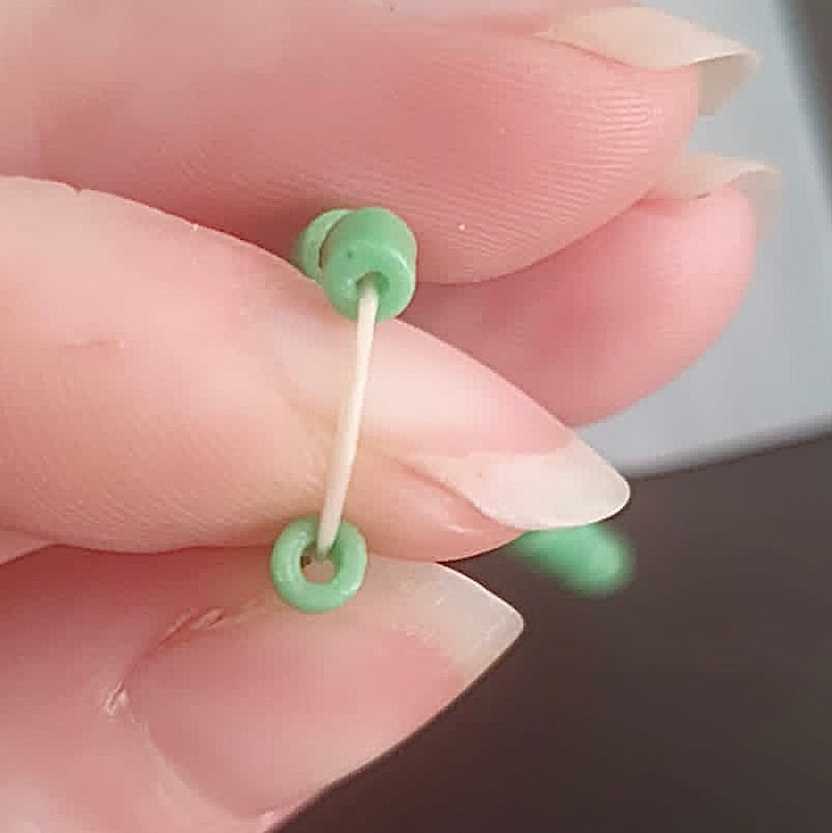 Close up of green beads on white elastic being held in fingers, to show threading hole in vintage sand cast green beads