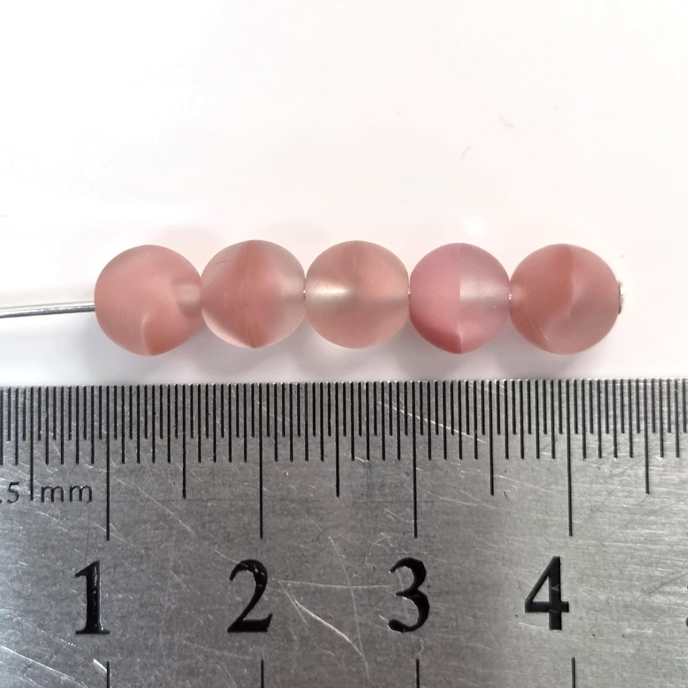 Pink beads on a metal ruler for size reference