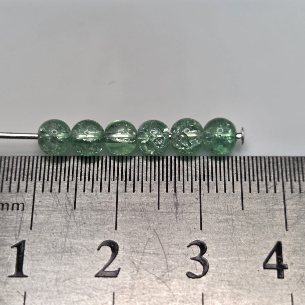 Green beads on a metal rod with a ruler for scale on a gray background