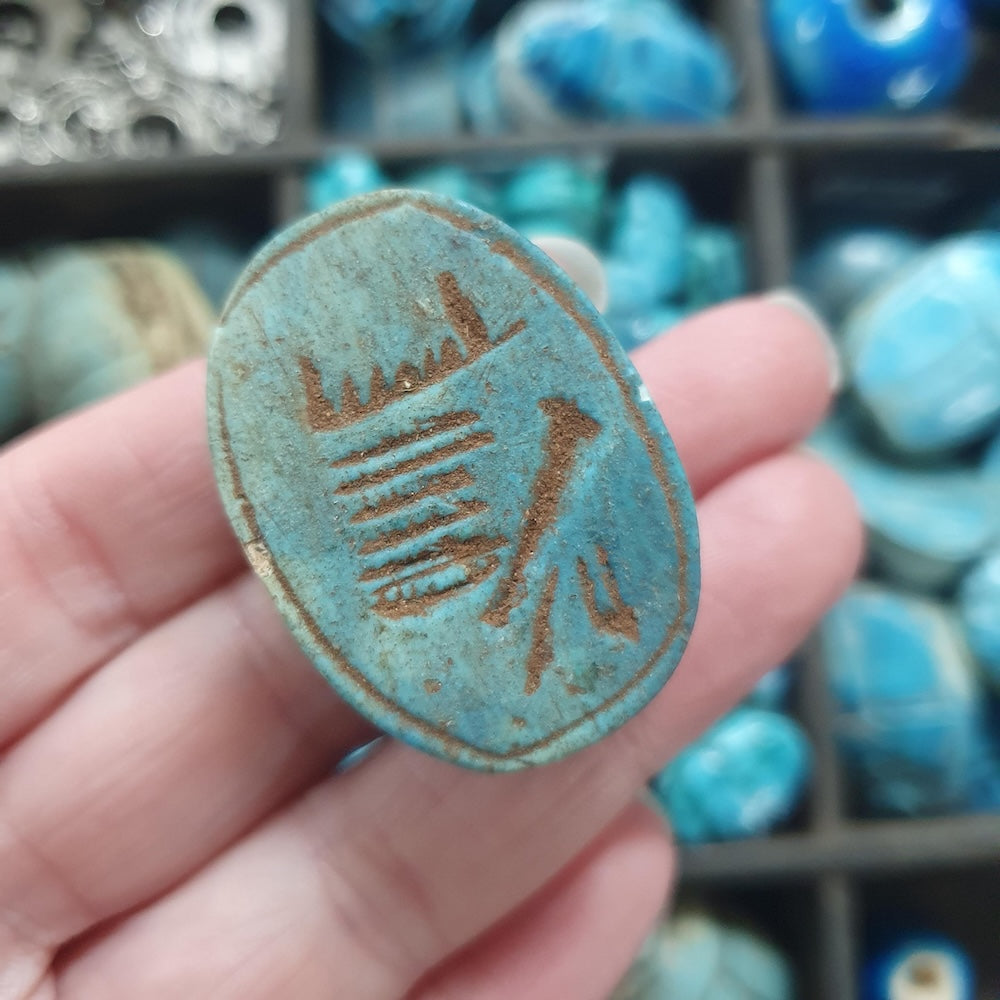 Turquoise scarab stone with brown design held in a hand, with more stones in the background