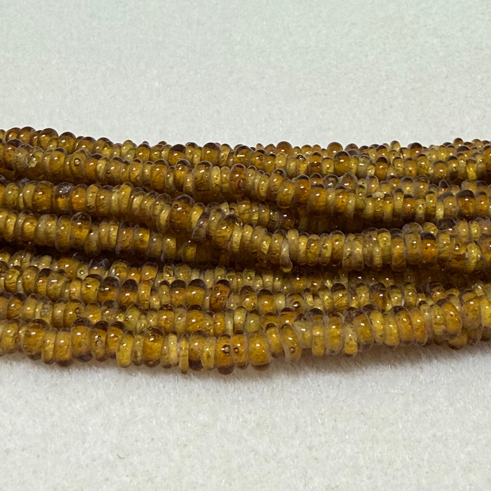 amber brown donut shaped Indonesian glass bead strands on a white background