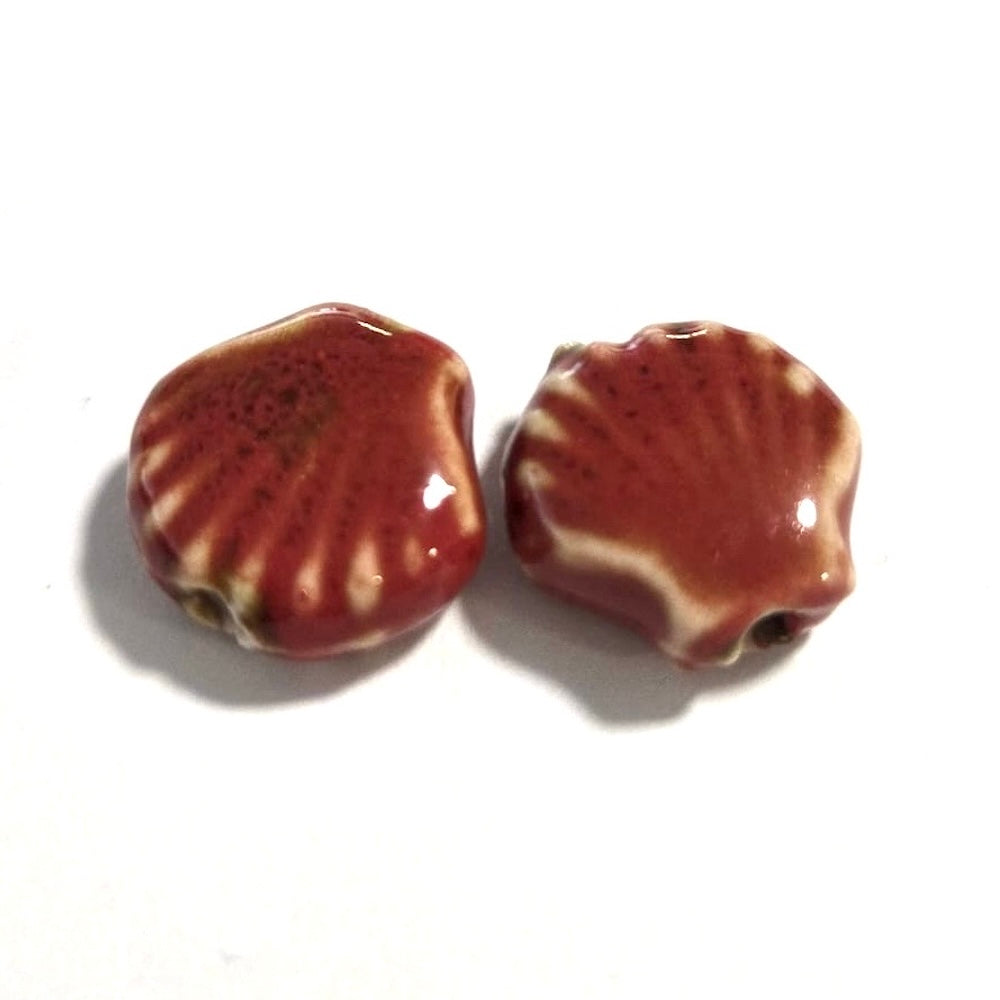 Two ceramic beads shaped like shells on a white background