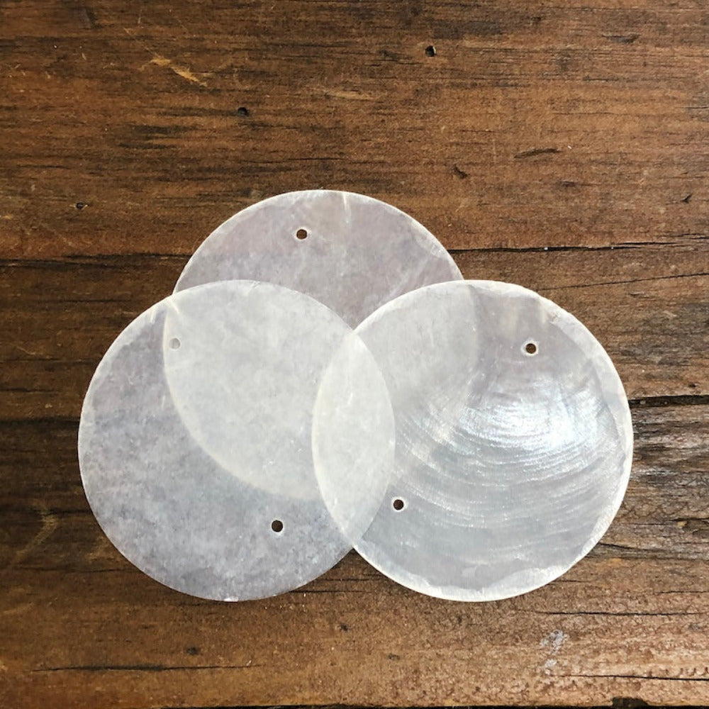 white capiz shell on a wooden surface used for wedding name cards, hanging decorations and craft items