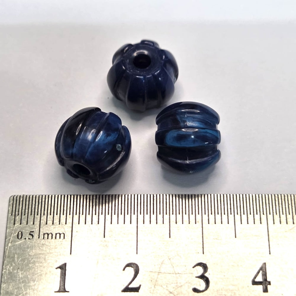 Three blue plastic beads with a ruler for scale on a white background