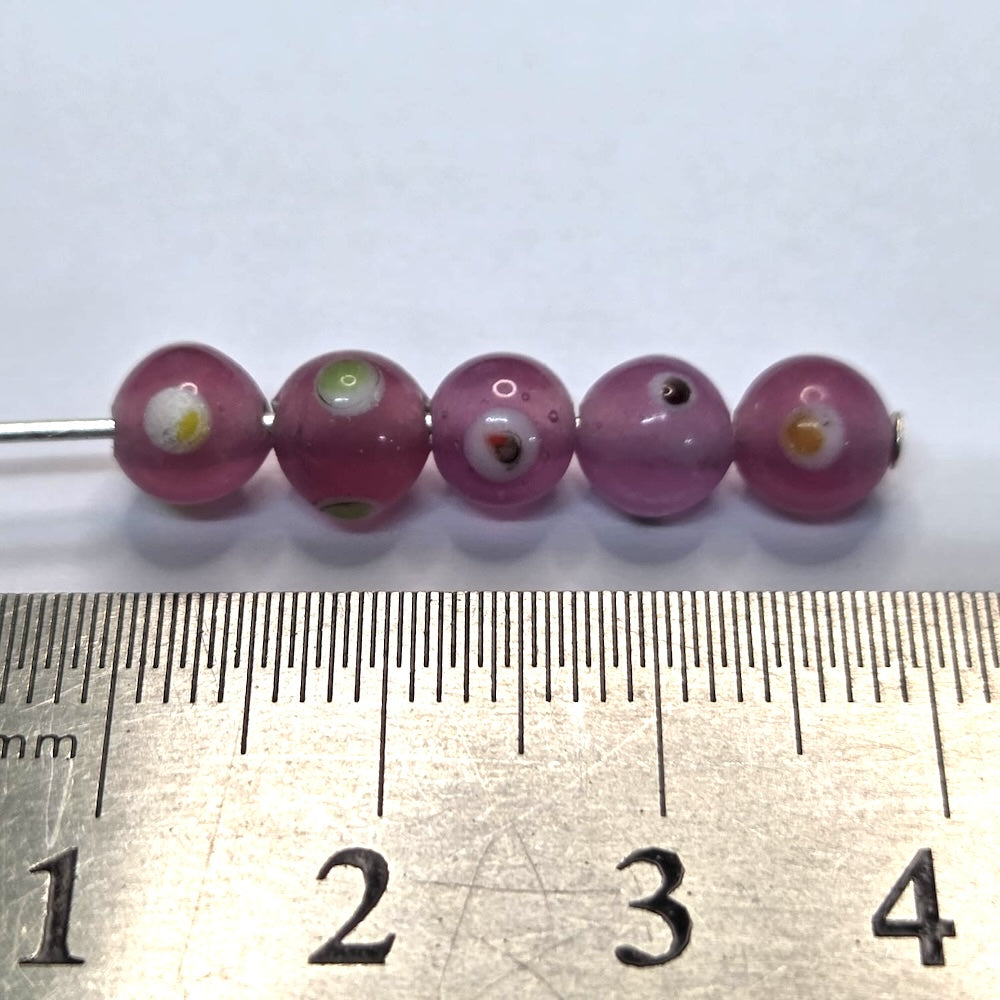 A collection of transparent pink glass beads with red yellow and white eyes, used for making jewelry with a ruler to show scale