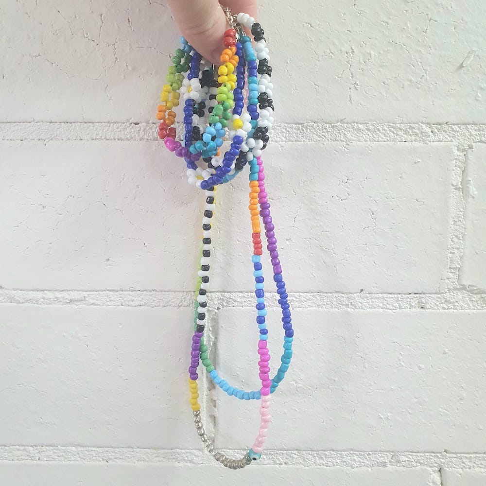 A hand holding colourful seed beaded bracelets and necklaces against a white background