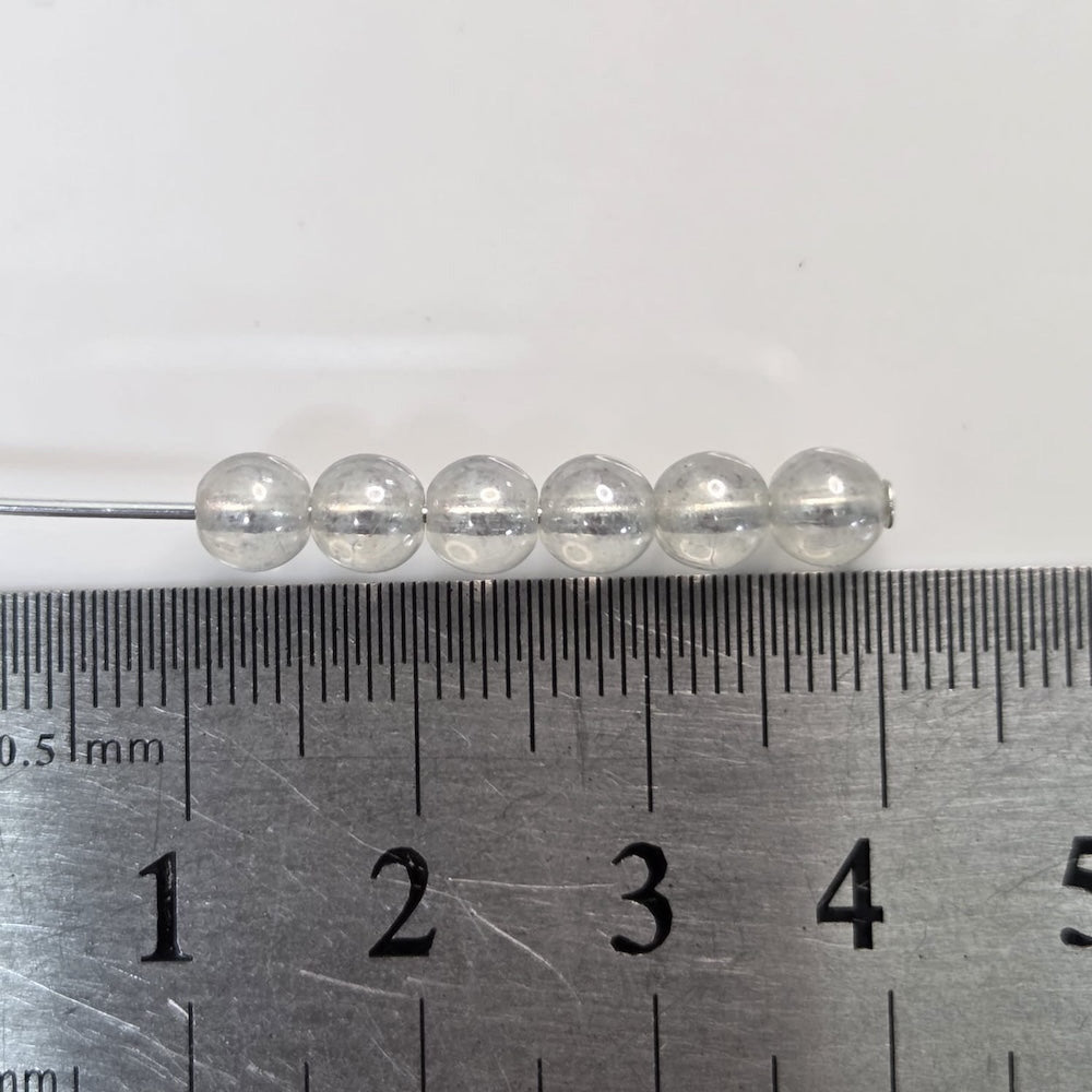 Clear beads on a pin with a ruler for scale on a white background