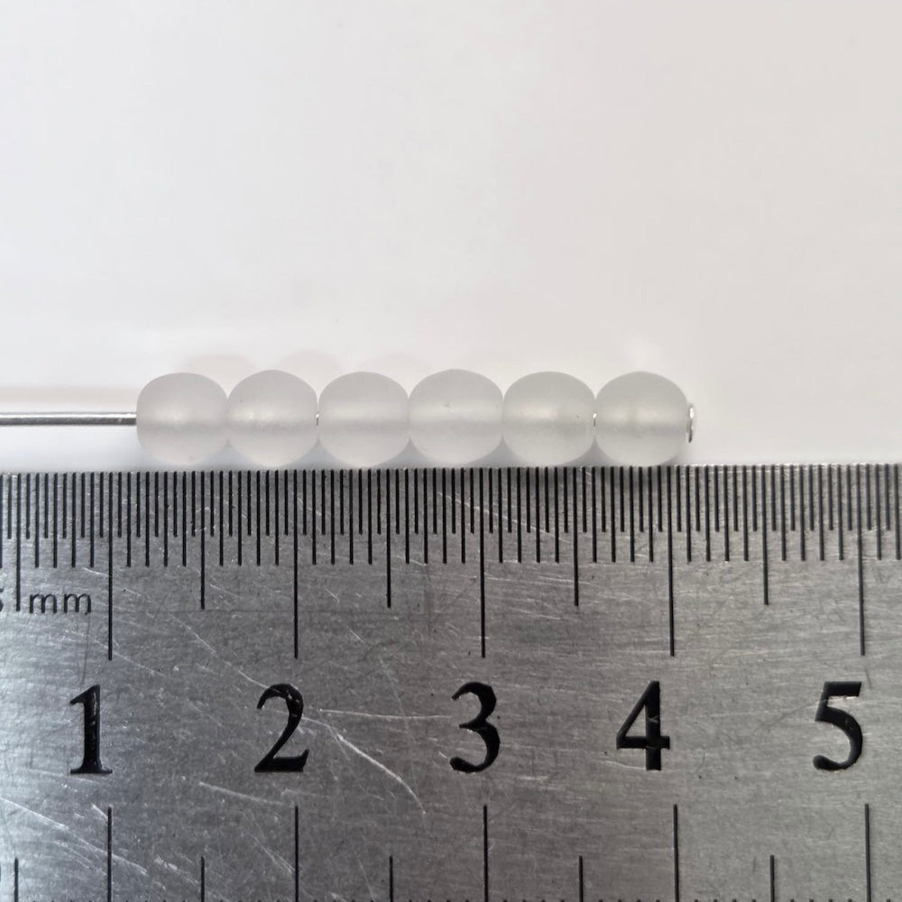 Metal ruler next to a row of white beads on a light gray background