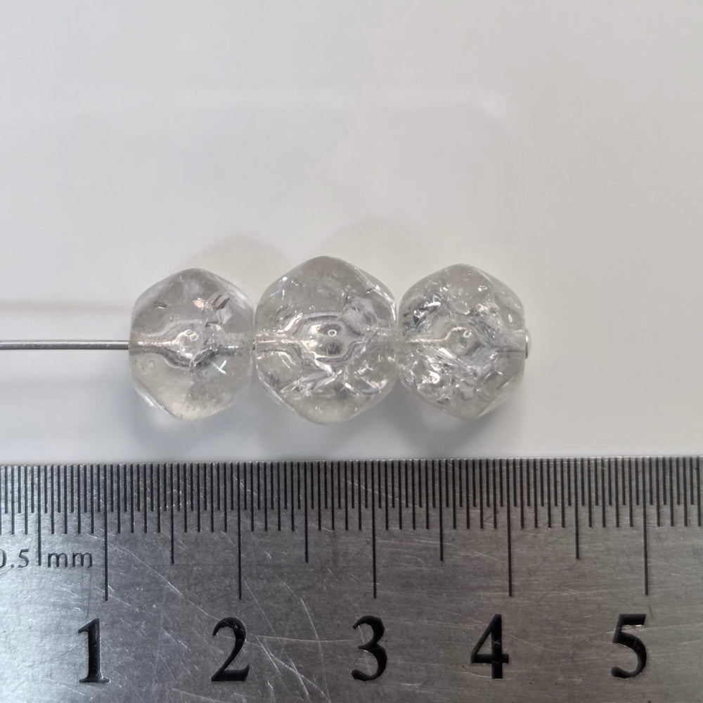 Three clear glass beads next to a ruler on a white background