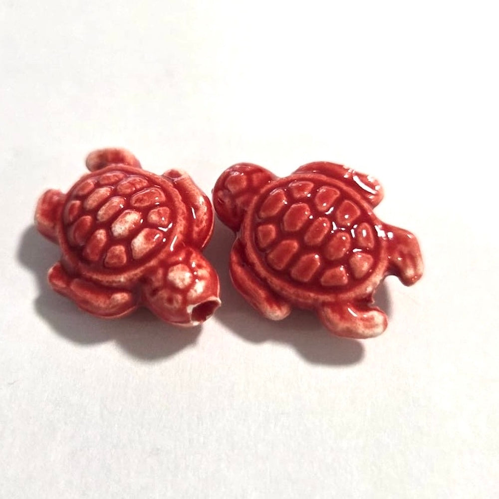 Two red turtle-shaped beads on a white background