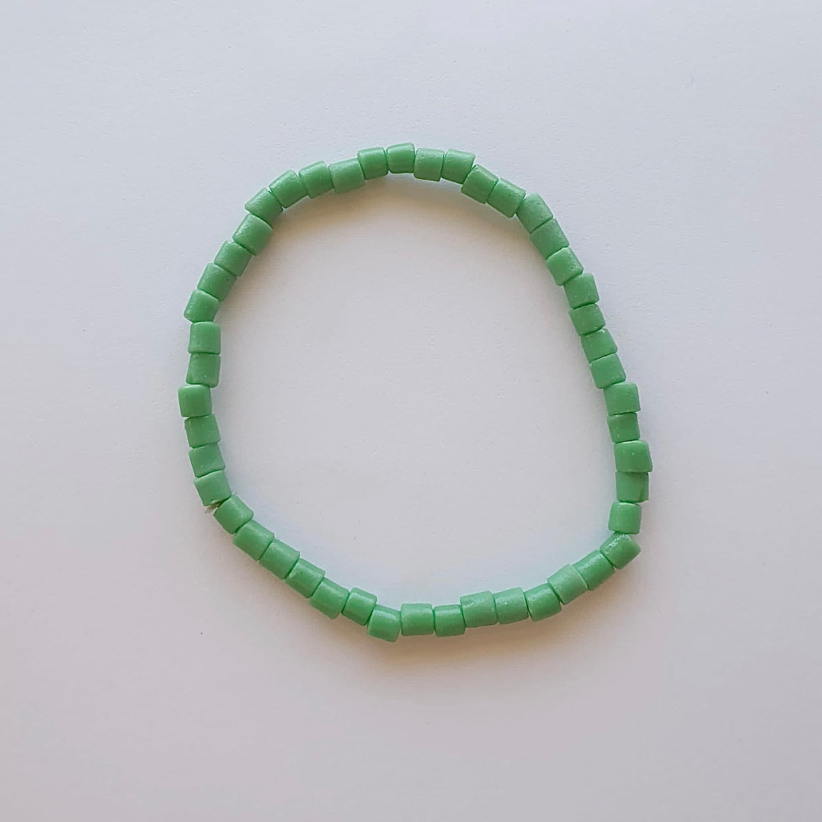 A bracelet on wrist showing vintage sand cast tube beads in green on a grey background