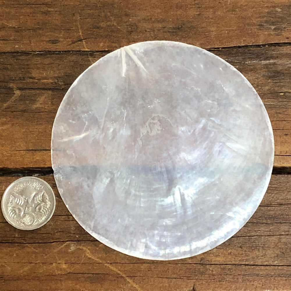 white, round capiz shell disc placed on a wooden surface used for wedding name place settings, bonbonniere, artwork and craft items displayed on a wooden surface next to a coine for size comparison