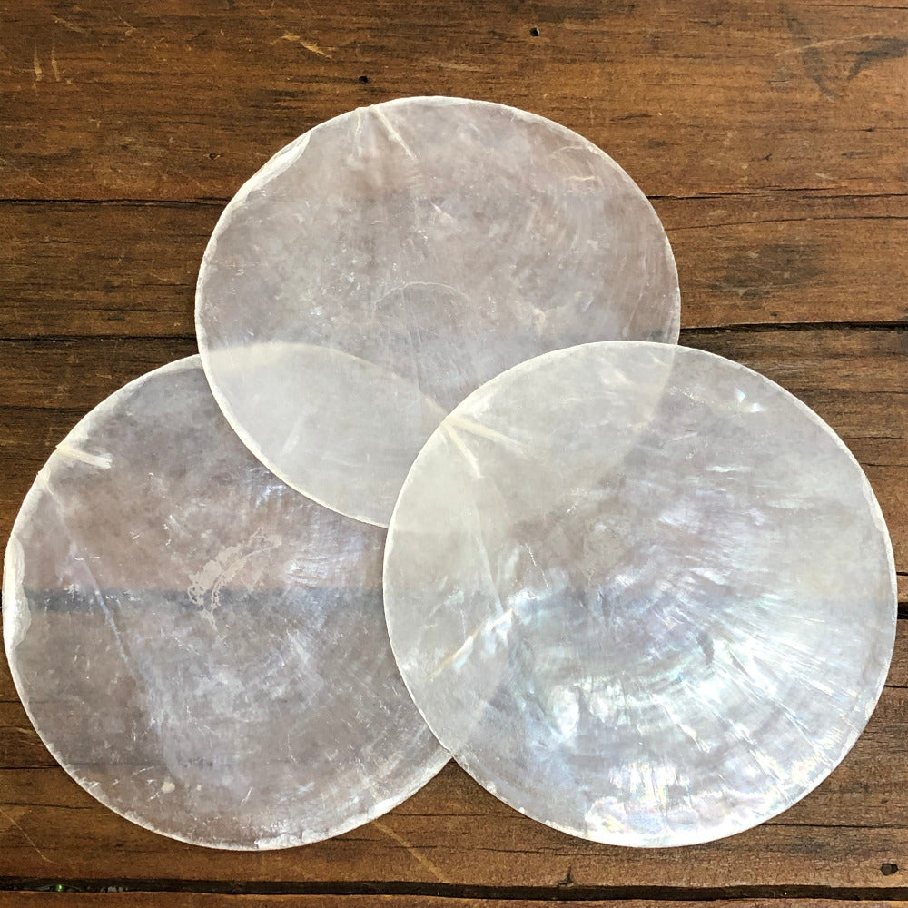 white, round capiz shell disc placed on a wooden surface used for wedding name place settings, bonbonniere, artwork and craft items displayed on a wooden surface