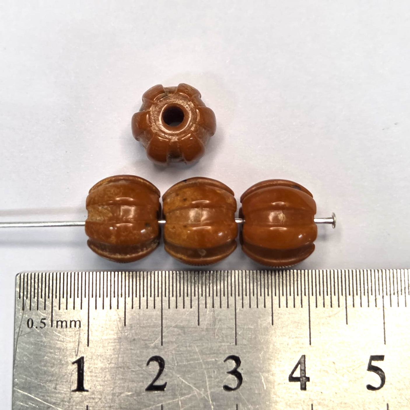 Brown beads on a metal rod with a ruler for scale on a white background