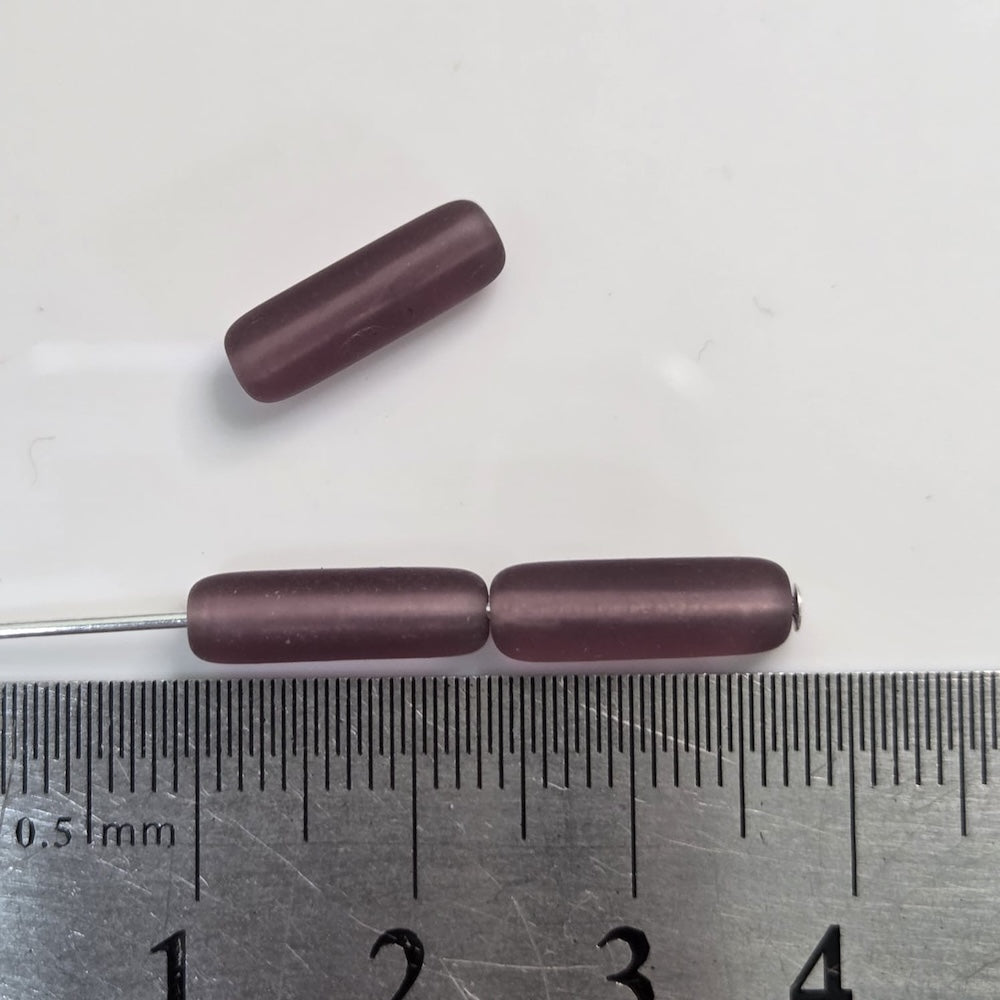 Three cylindrical purple beads on a metal rod with a ruler for scale on a white background