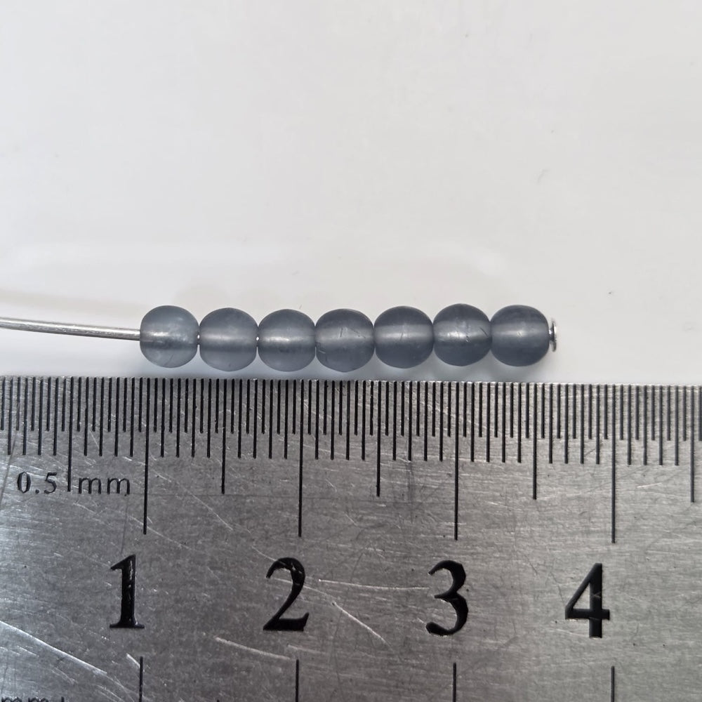 blue Gray beads on a needle with a ruler for scale on a white background