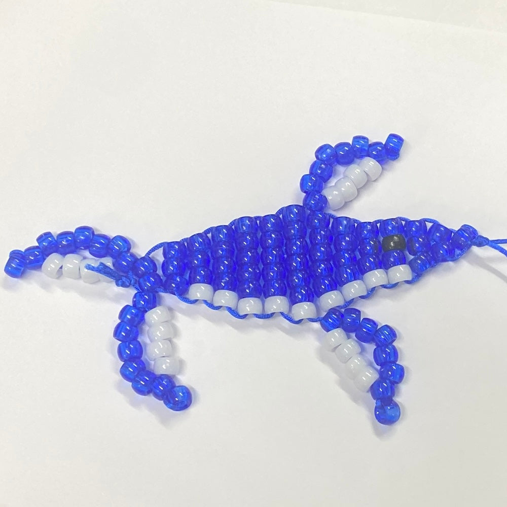 A blue and white beaded toy in the shape of a humpback whale made using a lace up kit.