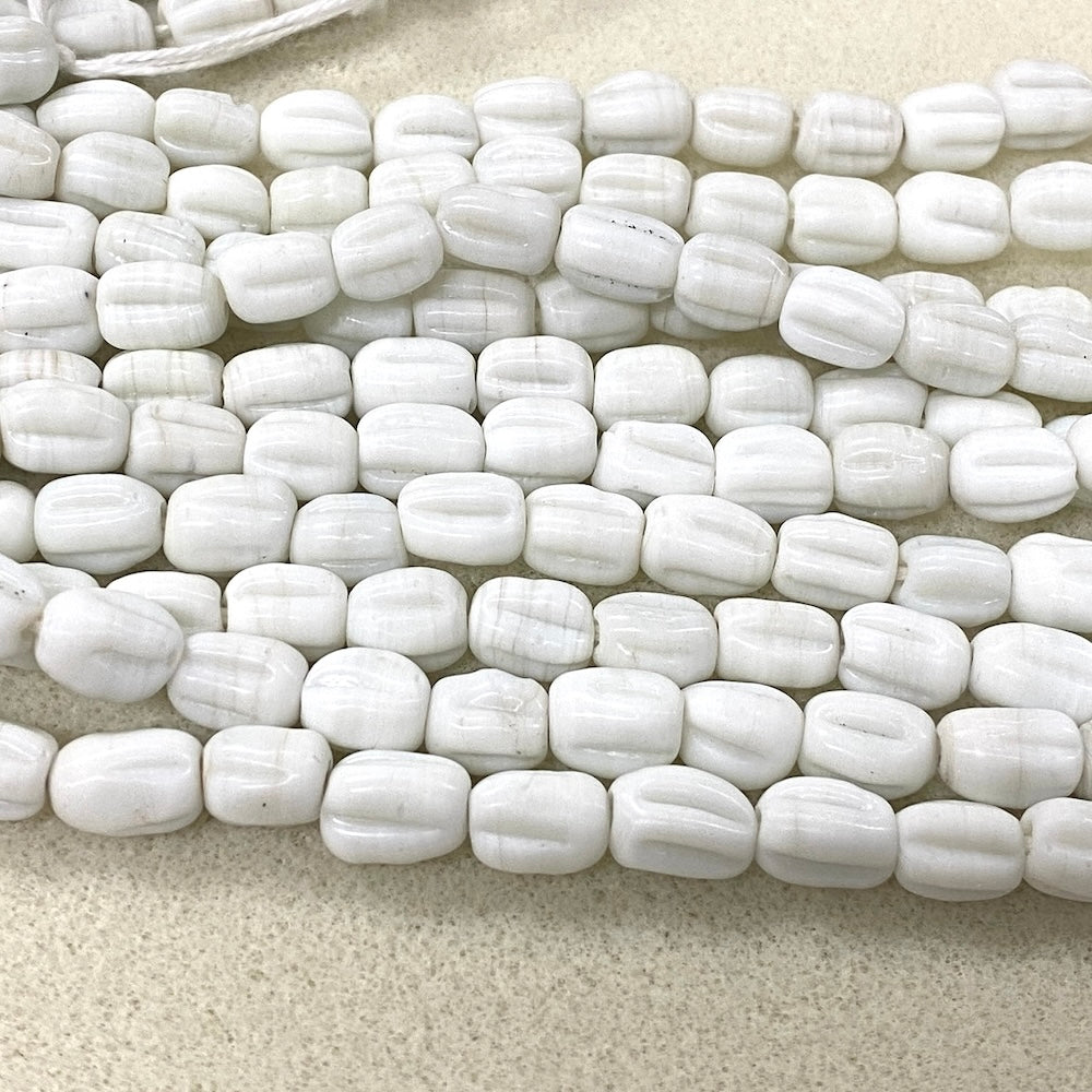 White ribbed cylindrical beads arranged in multiple rows on a light beige textured surface.