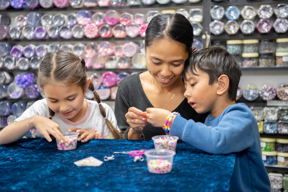 A mum and two children enjoying beading at a workshop table with jars of beads in the background