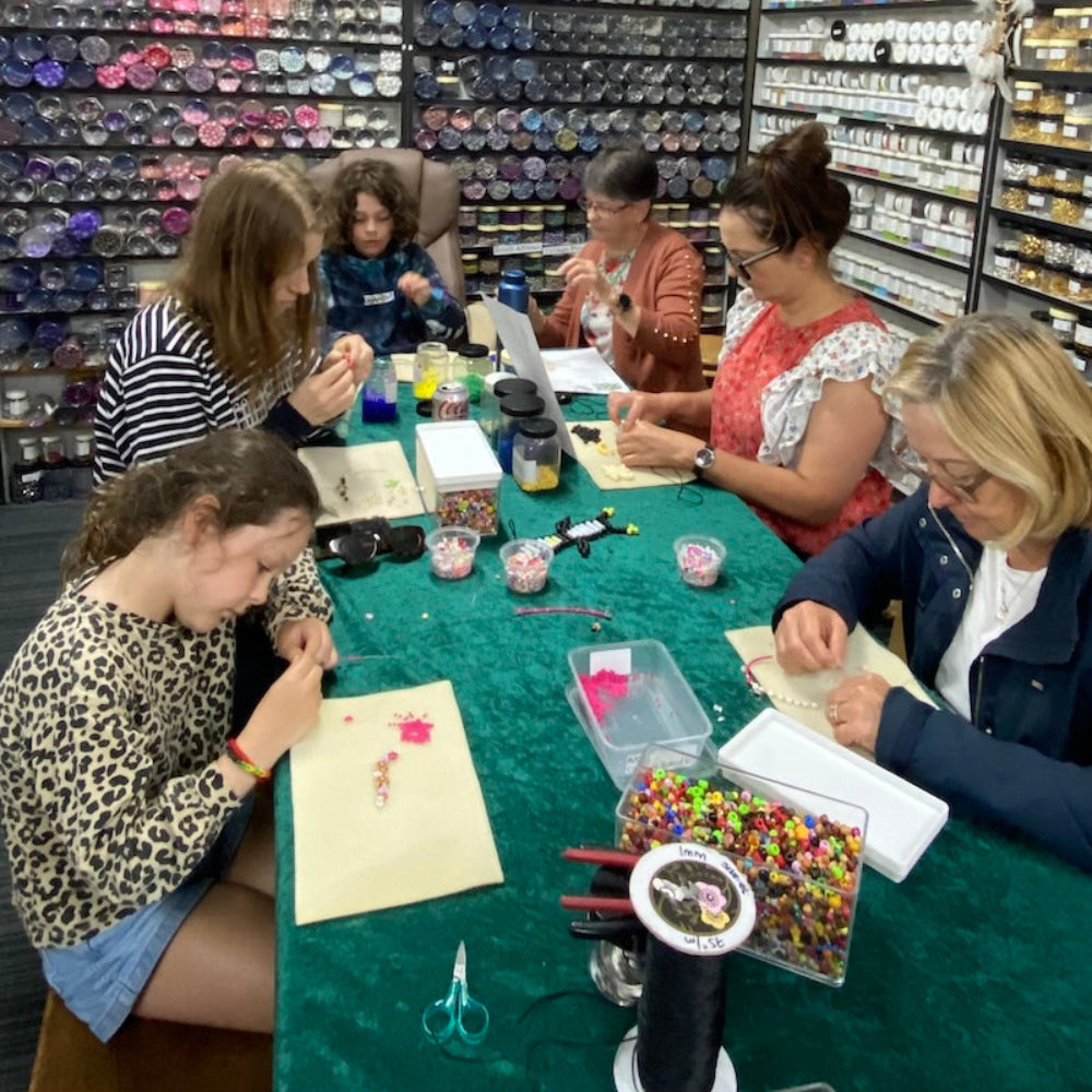 A group of people participating in a bead crafting workshop at Bead Shack, with various crafting materials displayed on tables.
