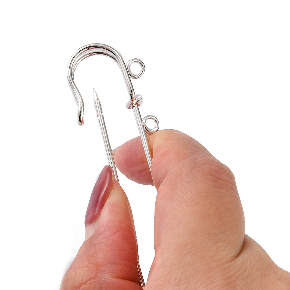 Kilt pin being held with fingers showing how to open the clasp in silver on a white background