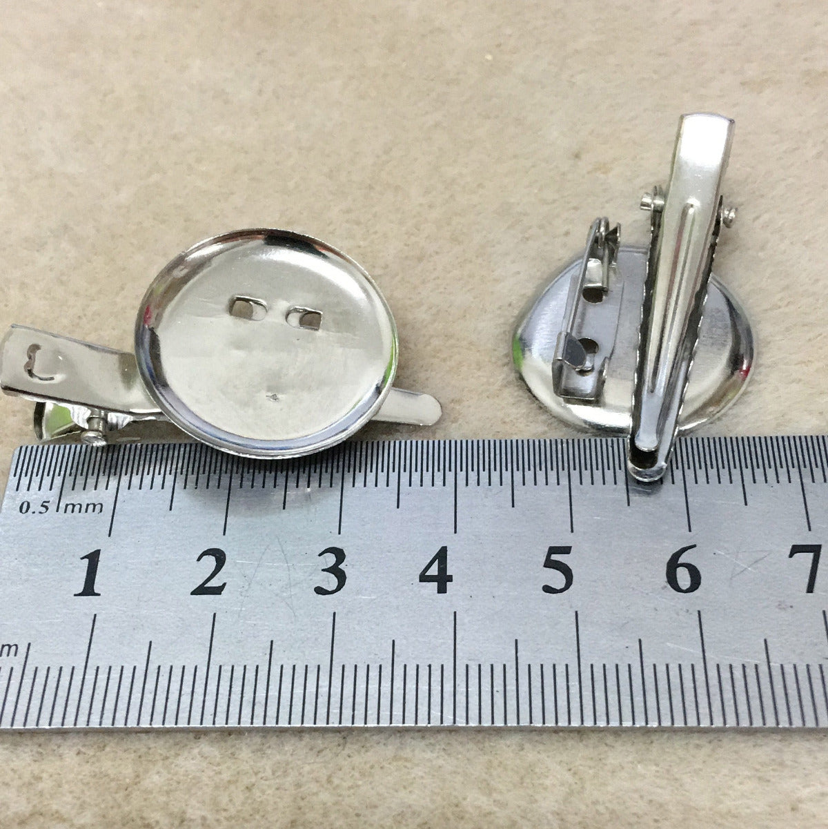 Two alligator style brooch settings on a textured fabric background with a ruler for scale.