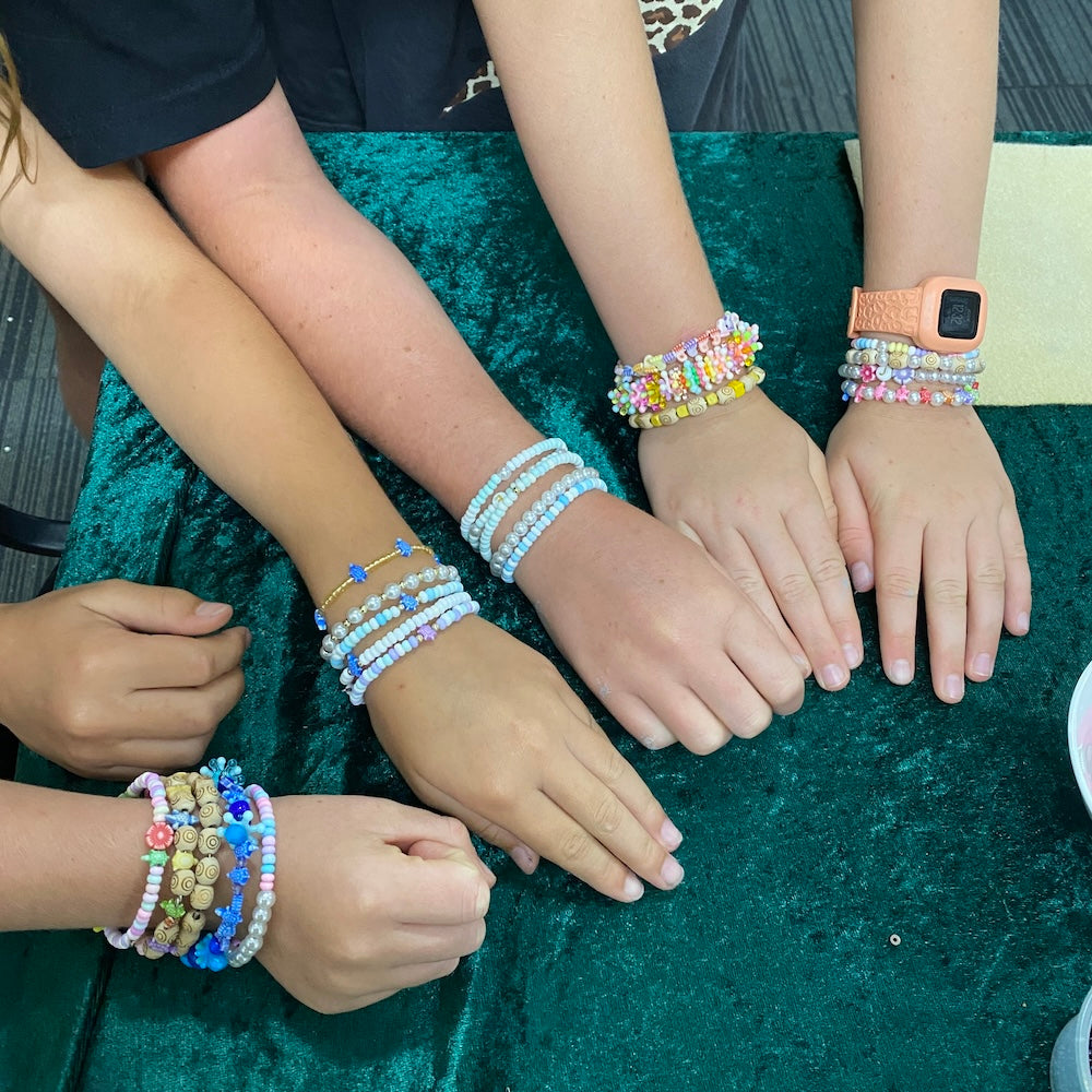 Children's hands wearing lots of colorful beaded bracelets on a green surface.