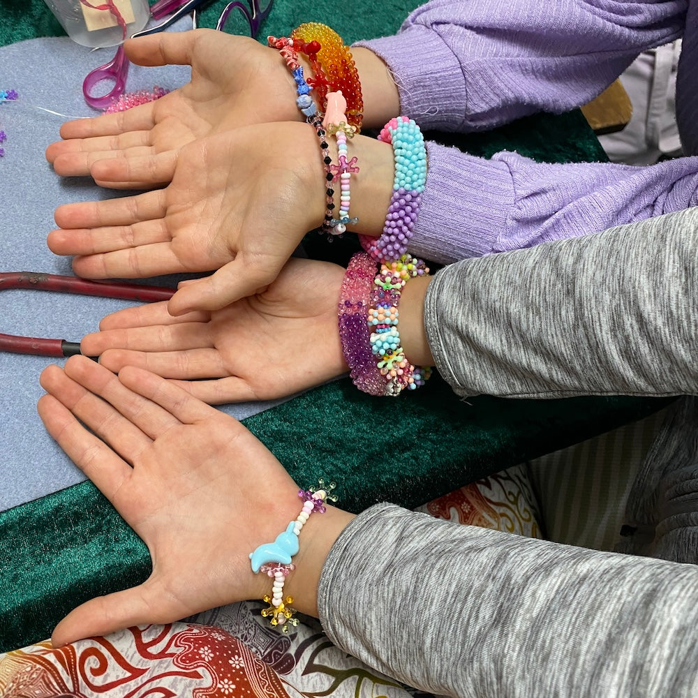 Hands wearing colorful beaded bracelets on a patterned surface