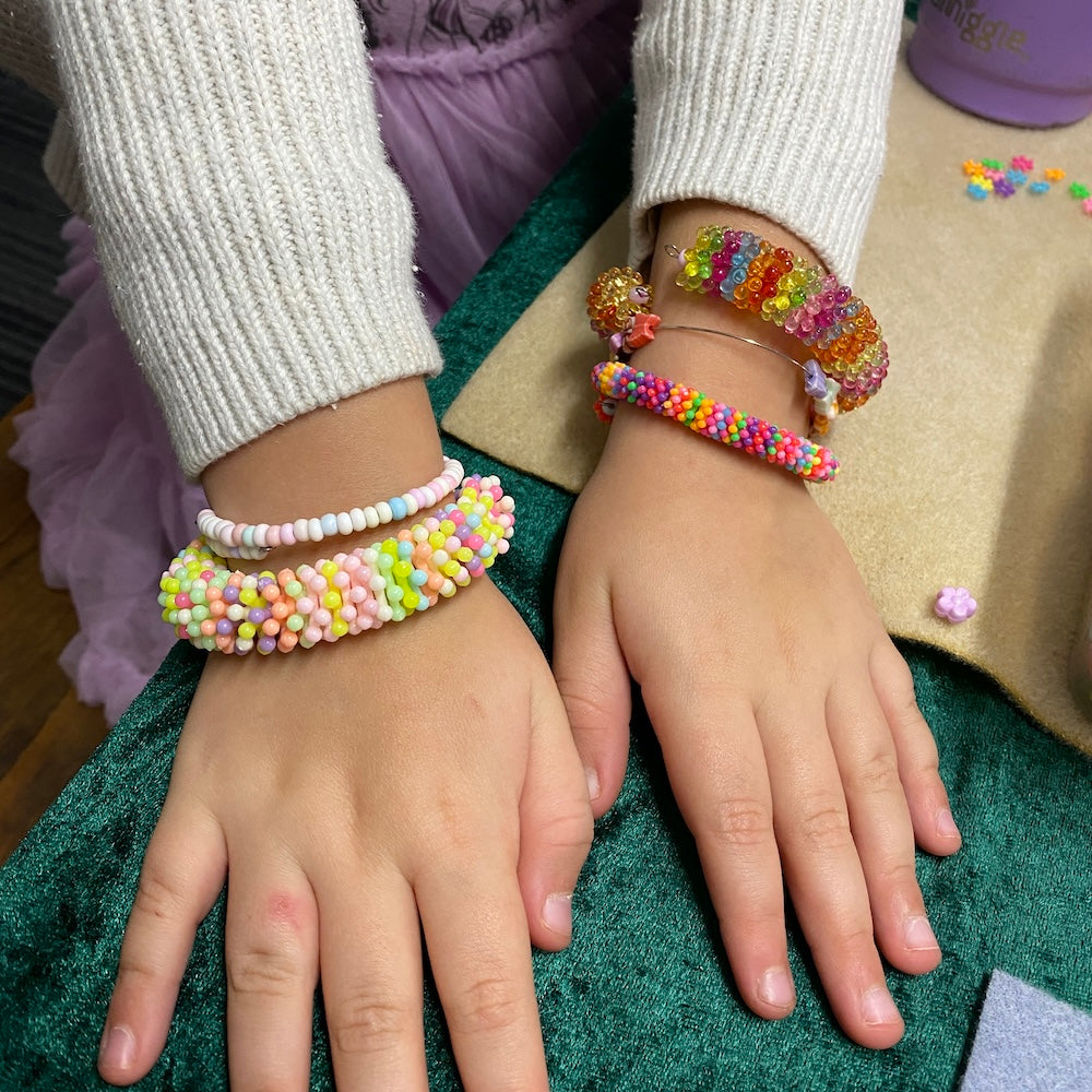Two hands wearing colorful beaded bracelets.