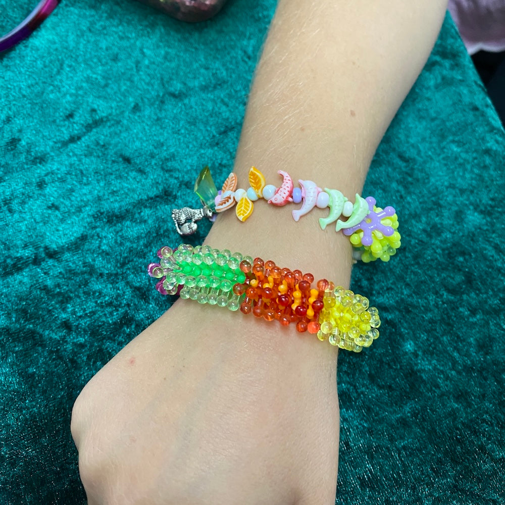 Colorful beaded bracelets on a wrist against a teal fabric background