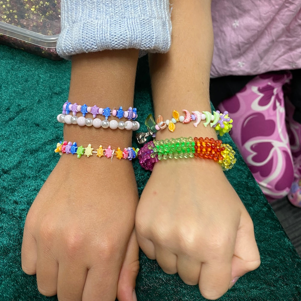 Two hands wearing colorful beaded bracelets showing dolphins leaves pearls and turtle beads.