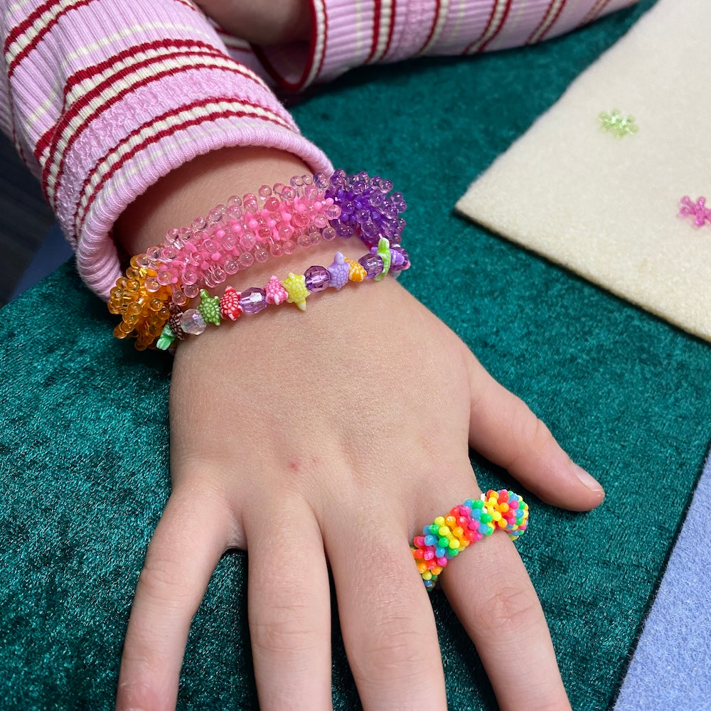 Hand wearing colorful beaded bracelets and a ring on a green surface