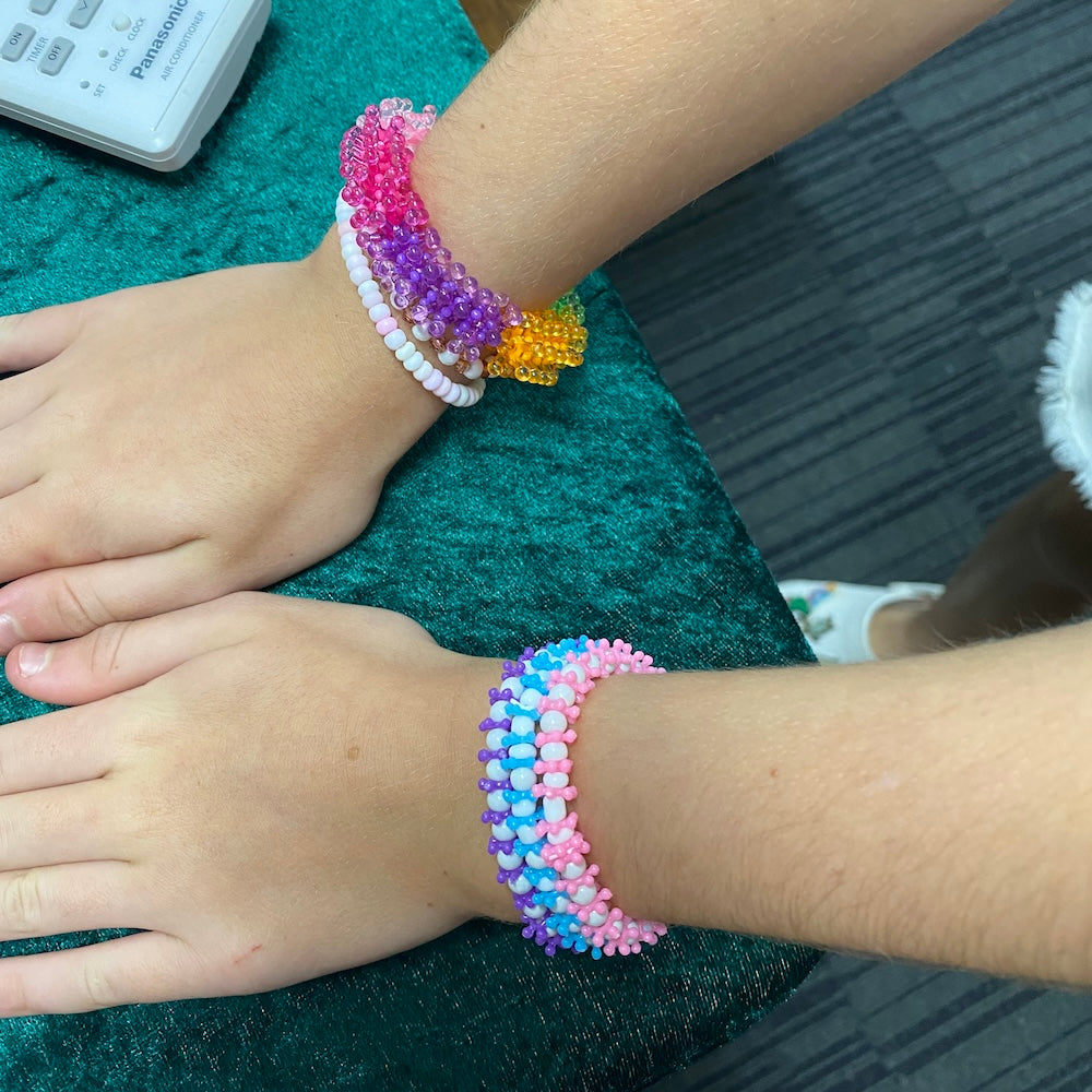 Colorful beaded bracelets on a person's wrists with a blurred background