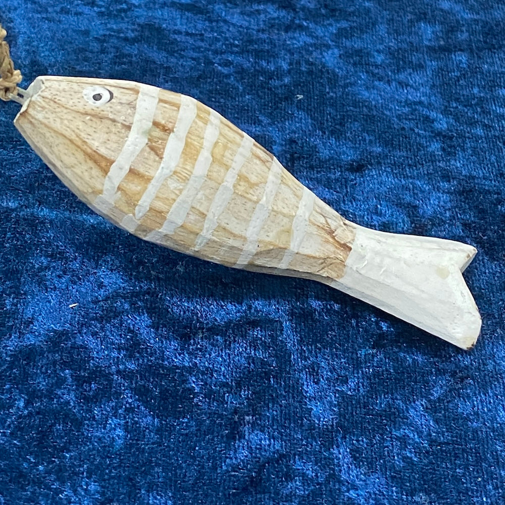 A hand-carved wooden fish decoration with a shabby chic white wash finish, displayed on a blue textured surface.