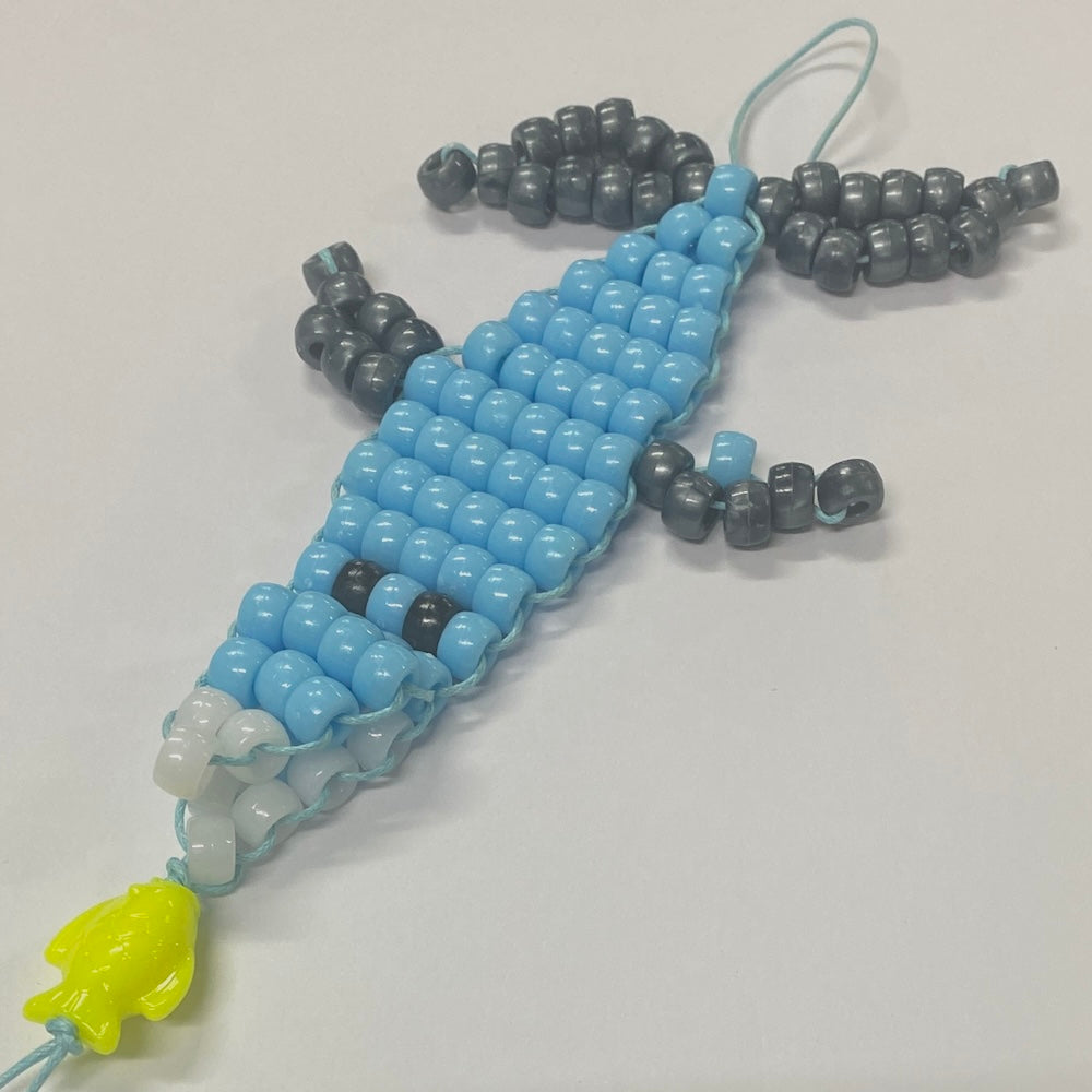 A completed bead weaving craft resembling a white pointer shark, made using blue and white beads on a cord.