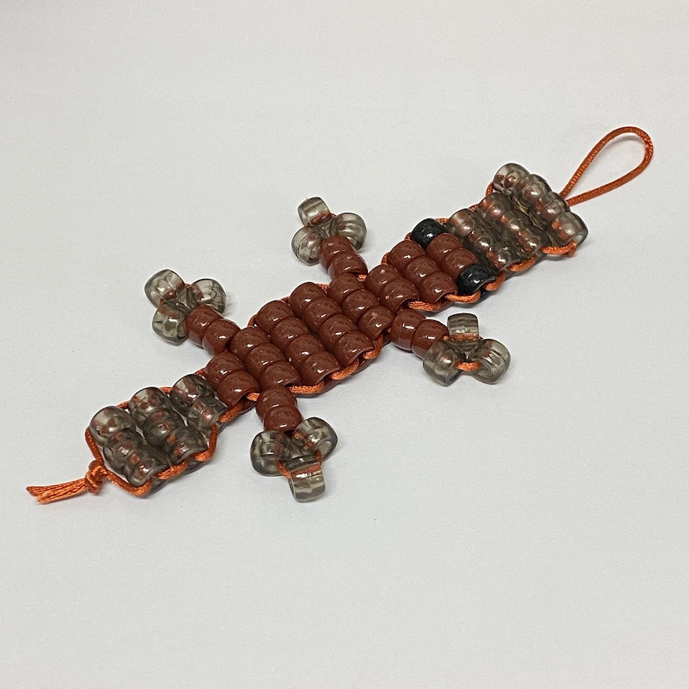 A handcrafted lace-up toy resembling a platypus, made from brown and black beads on a white background.