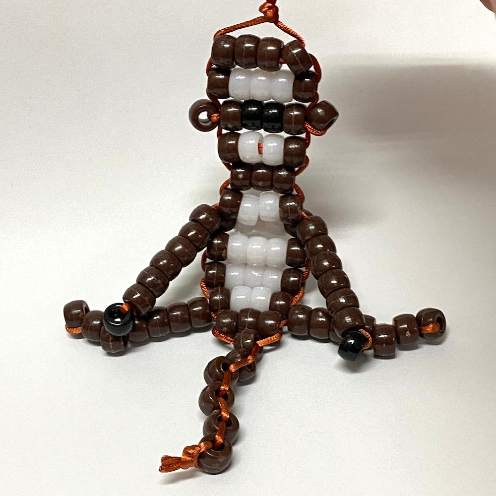 Beaded toy figure of a monkey made of brown, white, and black beads on a white background