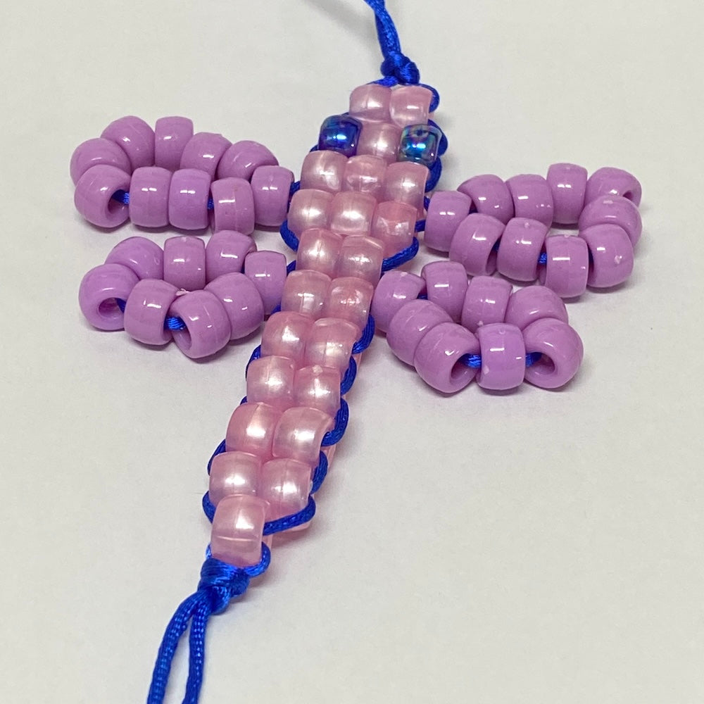A completed beaded craft project shaped like a dragonfly, featuring purple beads and blue cord.