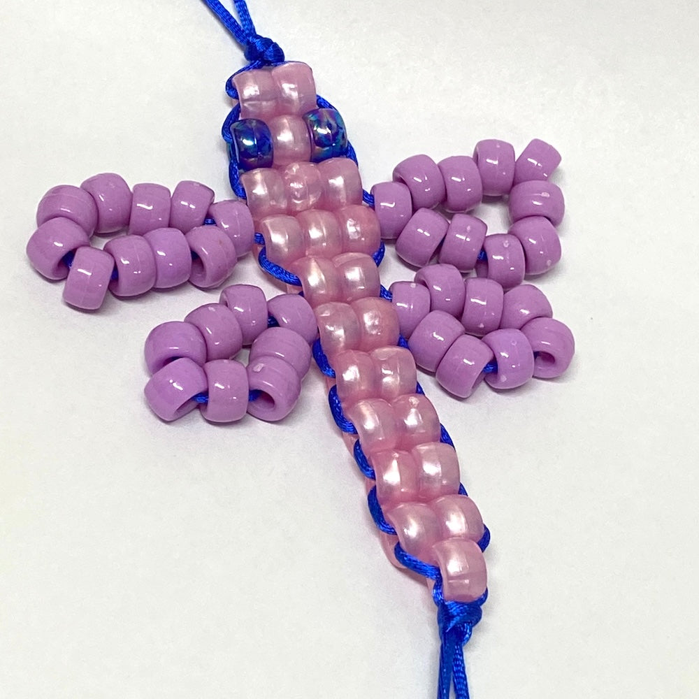 a beaded dragonfly kit toy with purple wings and pink body on a white background