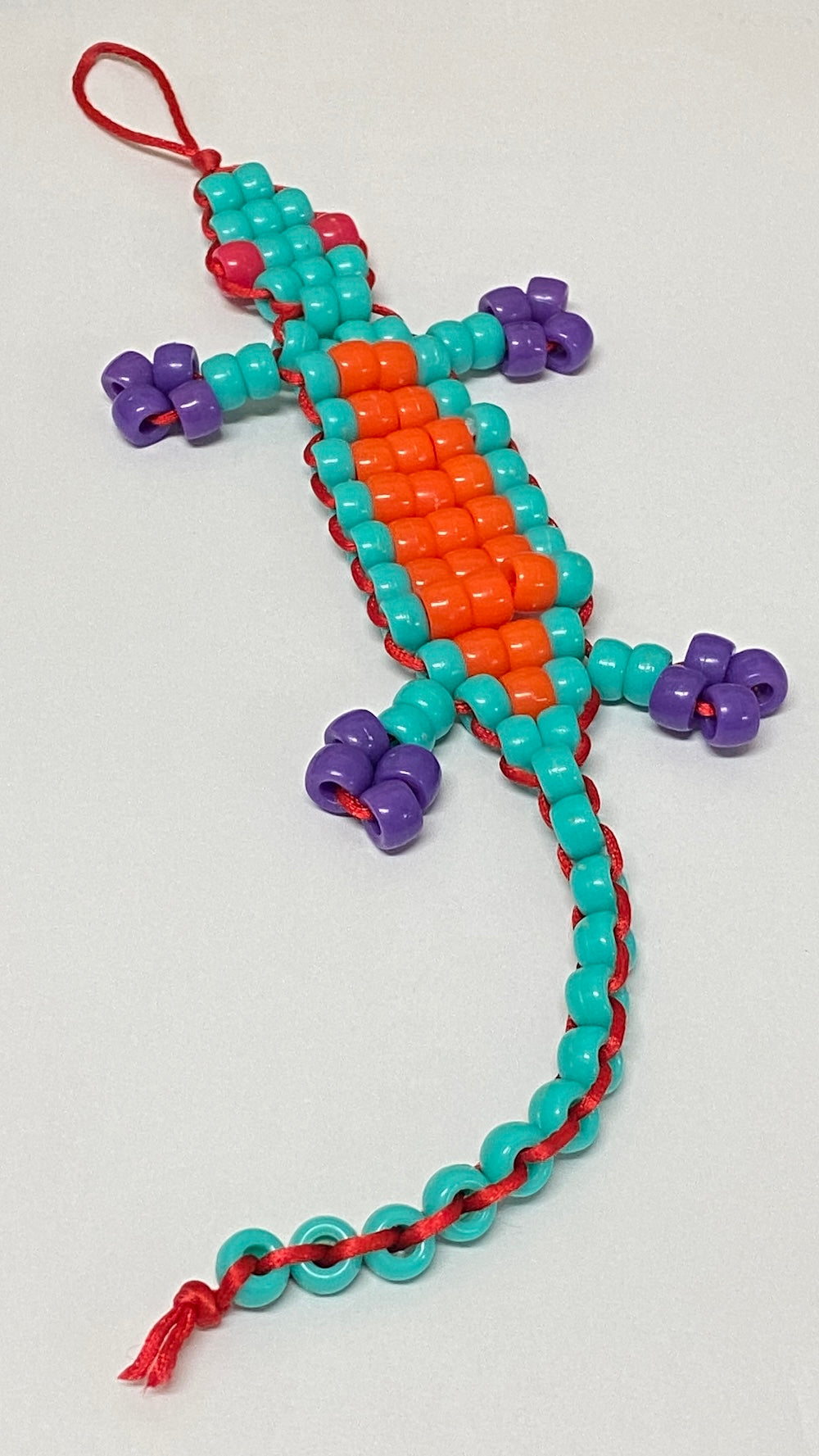 A handmade toy beaded gecko lizard kit with orange, teal, and purple beads on a white background.