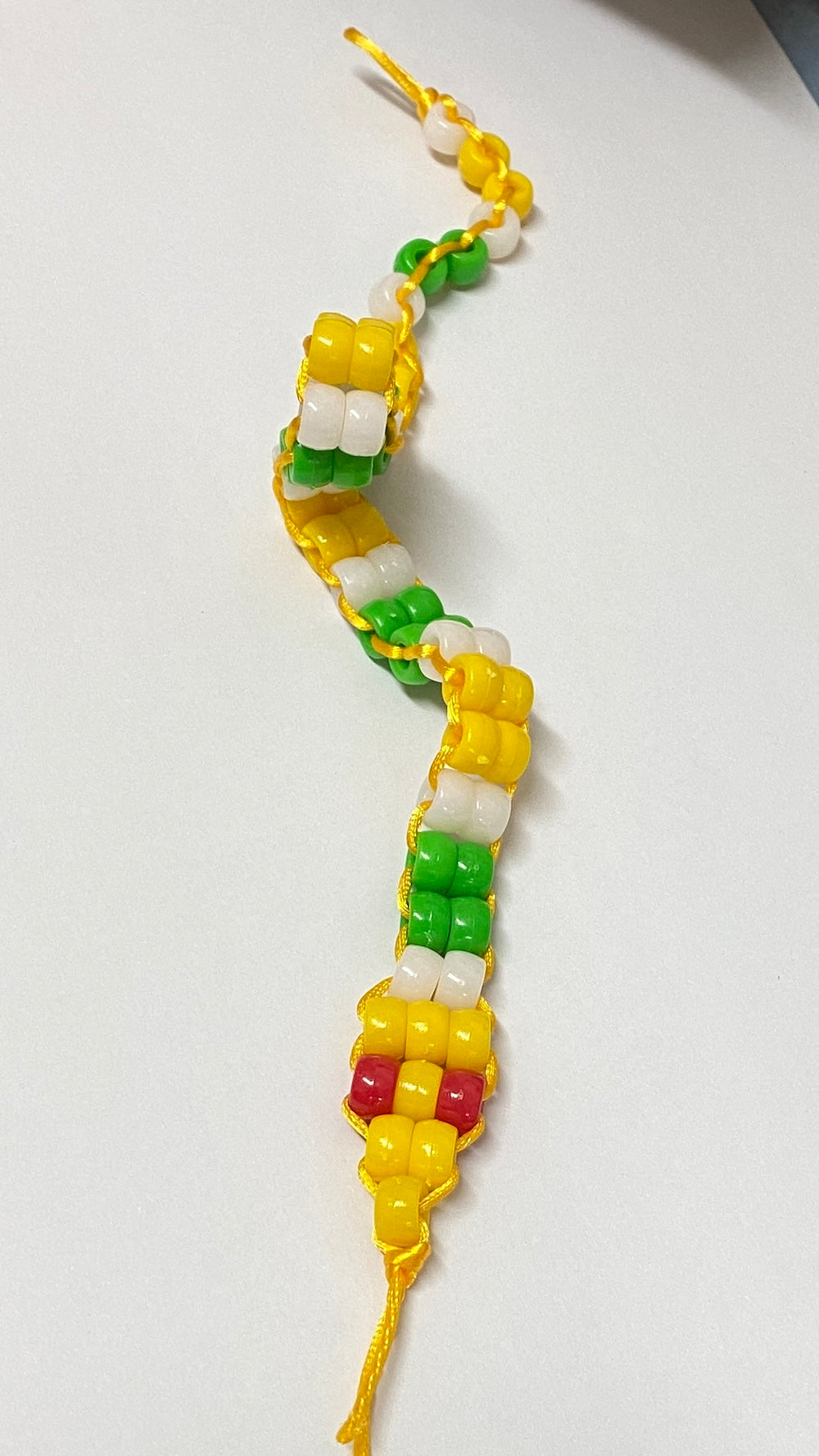 Colourful snake beaded toy made from a kit using pony beads in yellow green and white with red eyes on a white background