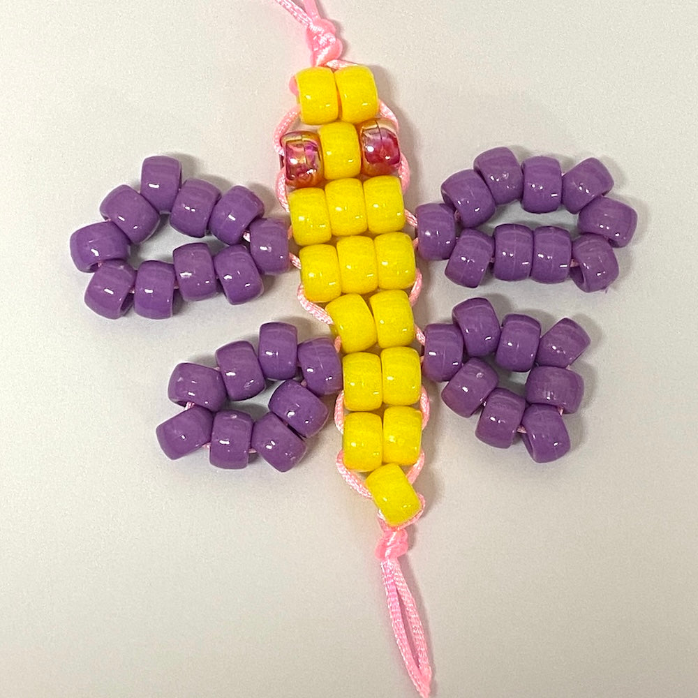 Beaded toy butterfly with yellow and purple beads on a pink string against a white background