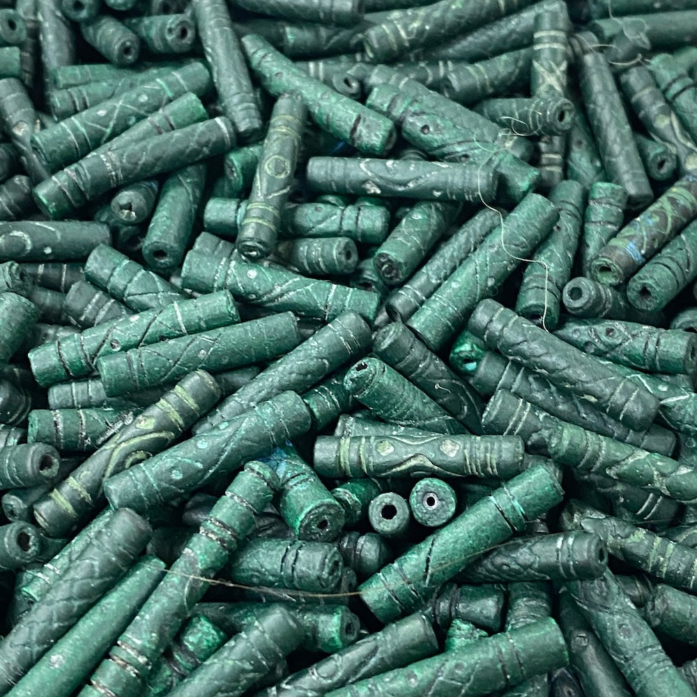 Close-up of a pile of green cylindrical vintage ceramic beads with intricate patterns.