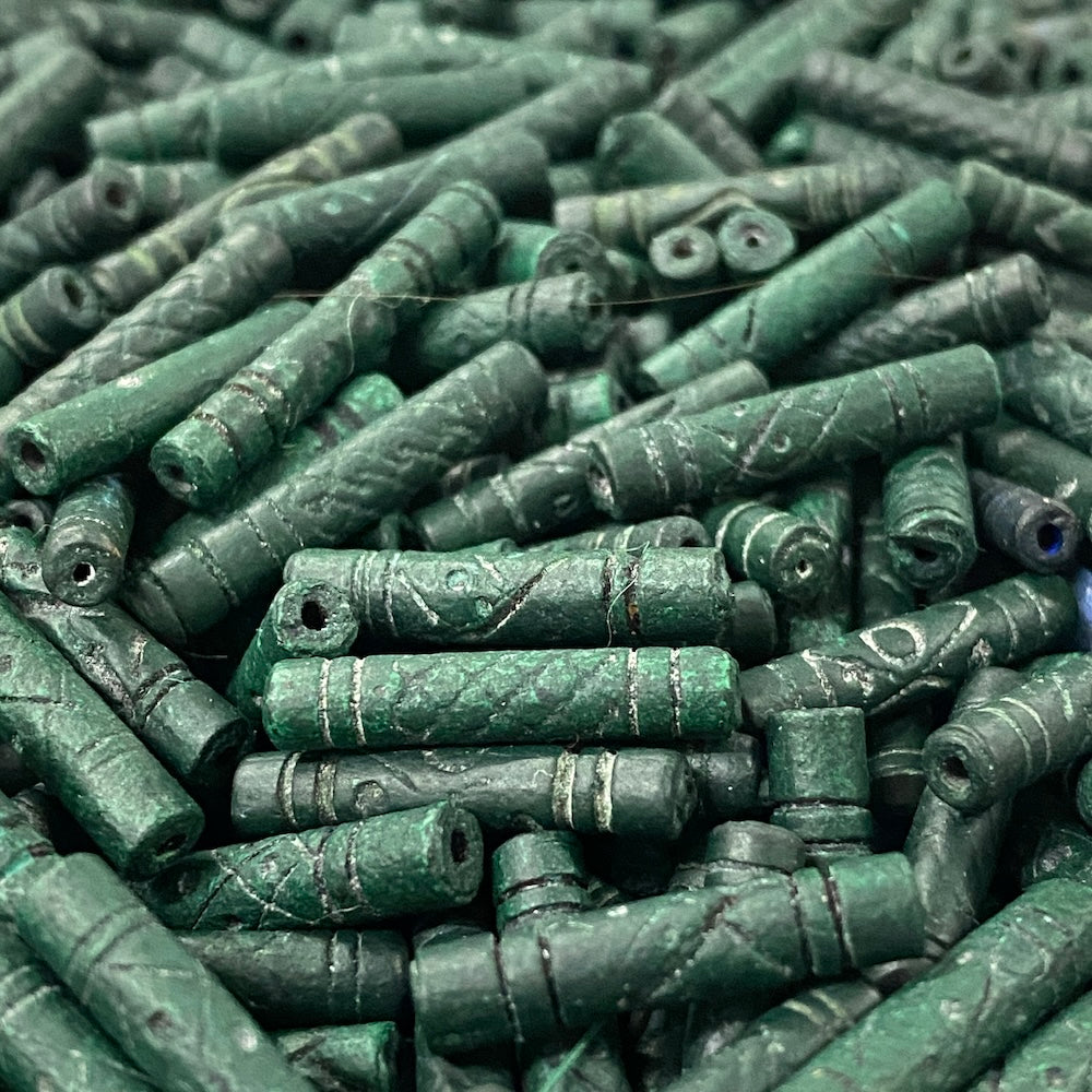Close-up of a pile of green cylindrical vintage ceramic beads with intricate patterns.