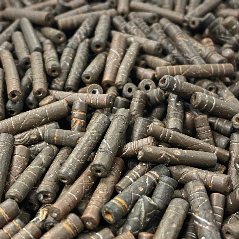 Close-up of a pile of dark brown cylindrical vintage ceramic beads with intricate patterns.