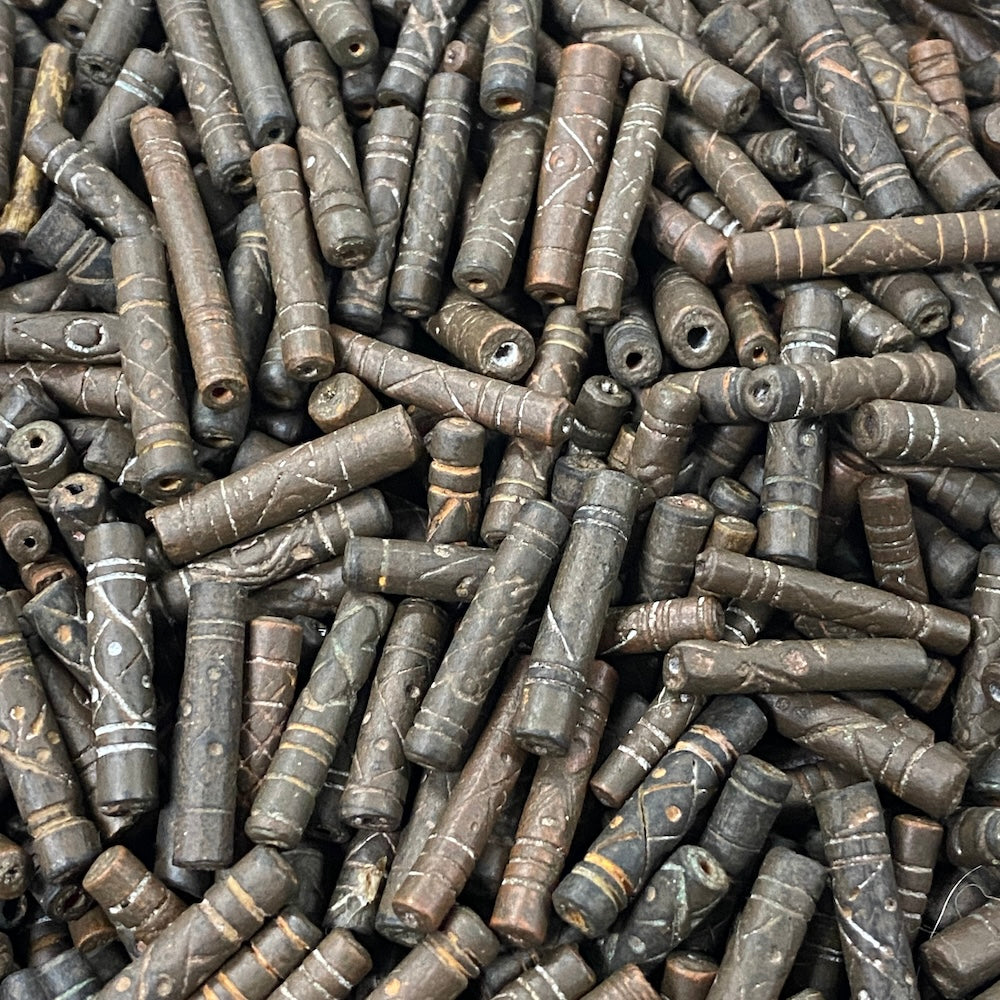 Close-up of a pile of dark brown cylindrical vintage ceramic beads with intricate patterns.