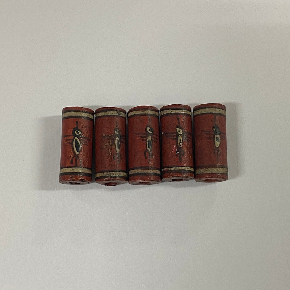 Five cylindrical vintage ceramic beads with decorative patterns on a white background